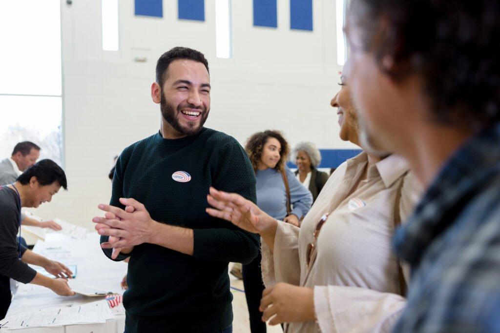 Cheerful mid adult Hispanic man smiles and laughs with friends as they wait to vote on election day.