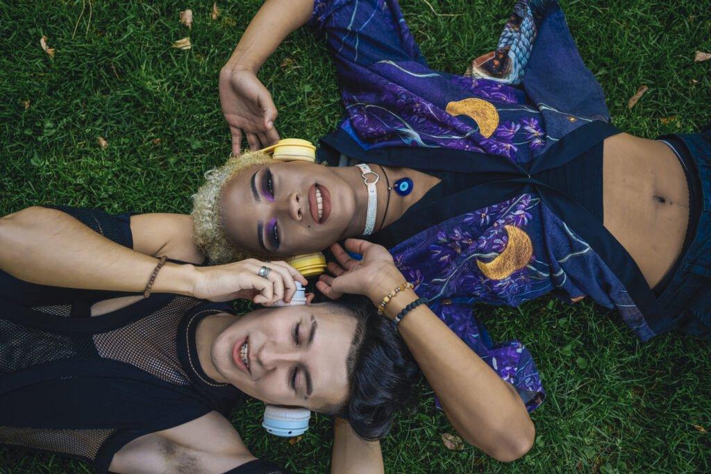 Two members of the LGBTQ+ community lying in grass listening to music.